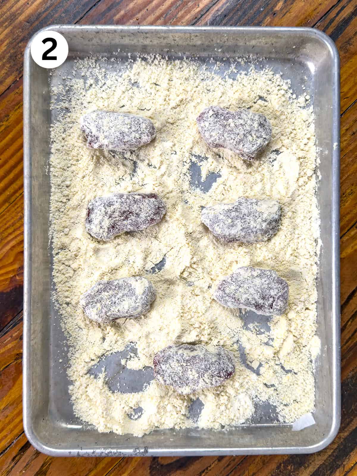 Venison backstrap coated in cornmeal on a baking sheet.