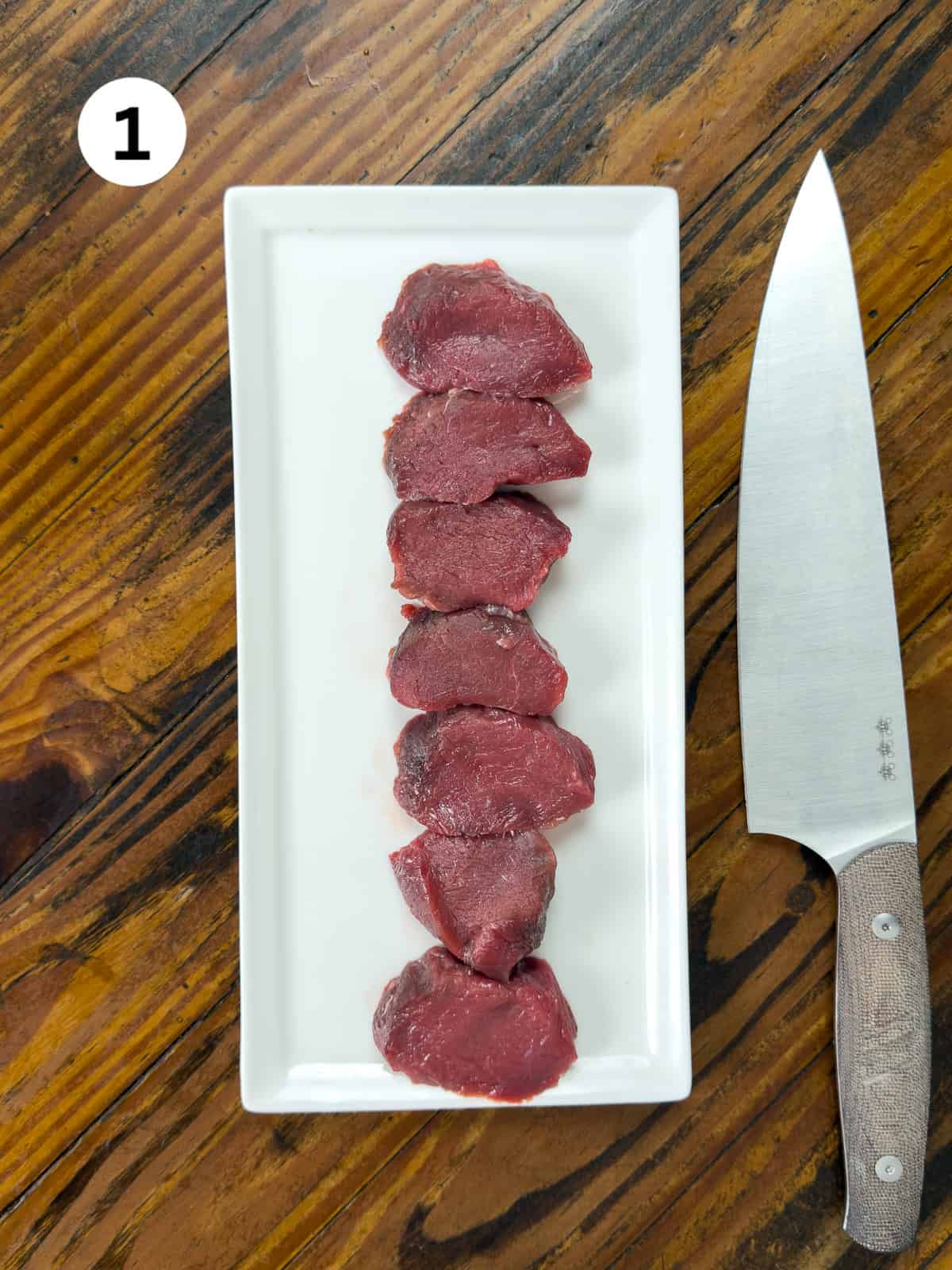 Venison backstrap cut into medallions on a wooden table with a knife.