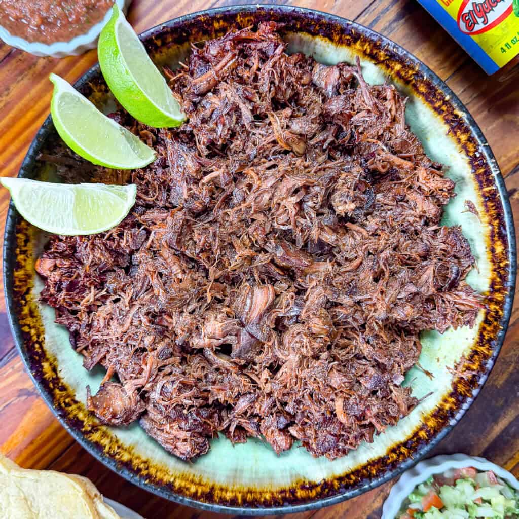 Venison barbacoa recipe in a bowl with limes