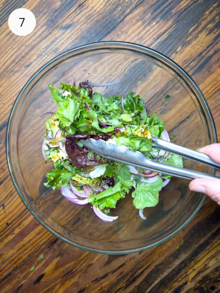 Tossing a Thai salad in a bowl with tongs.