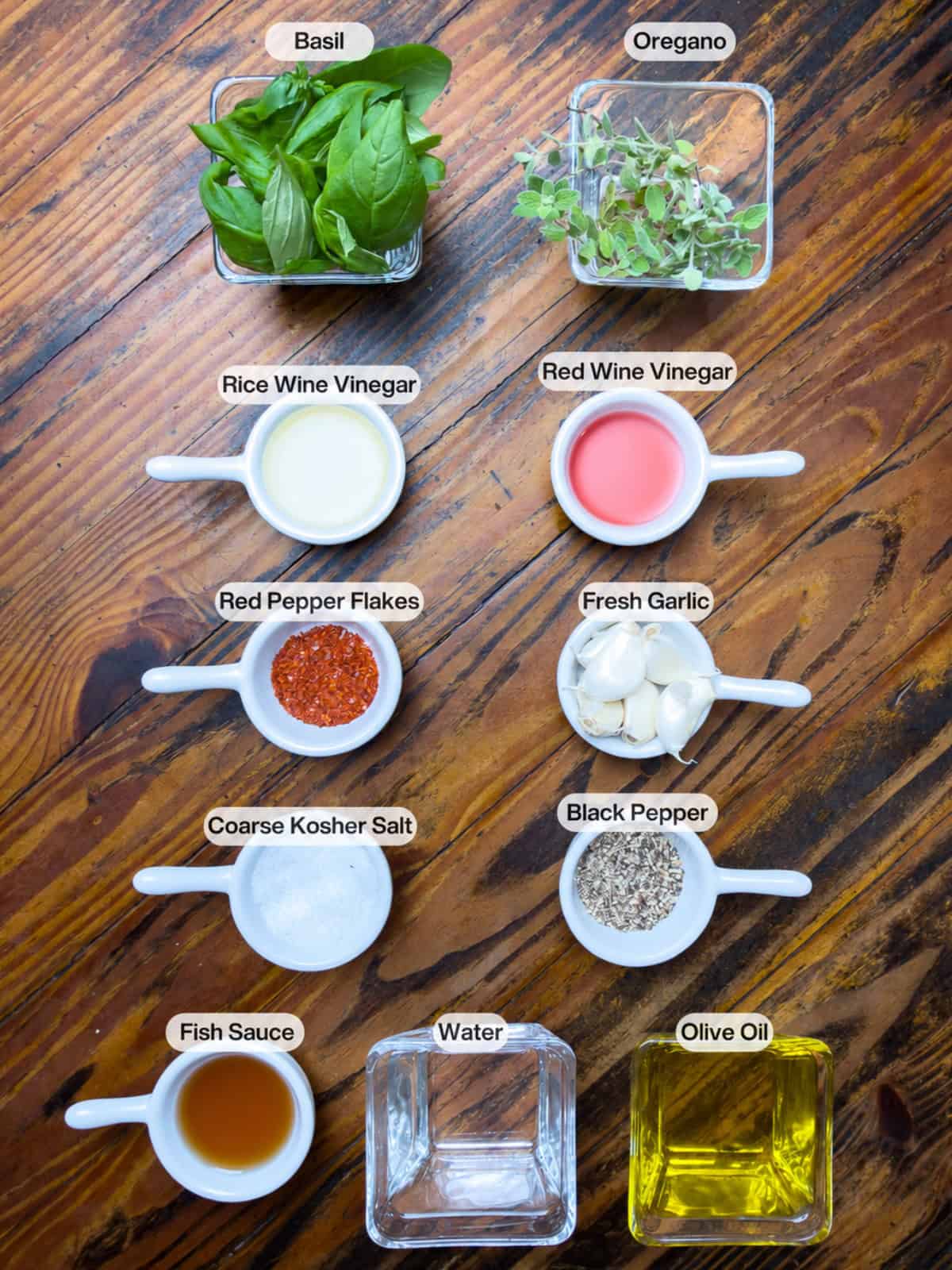 Basil chimichurri ingredients in dishes on top of a wooden table.