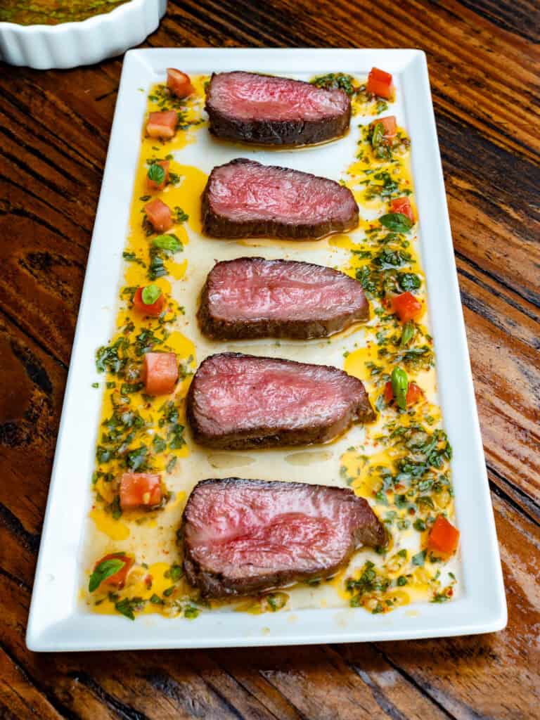 Basil chimichurri with a venison steak on a white plate