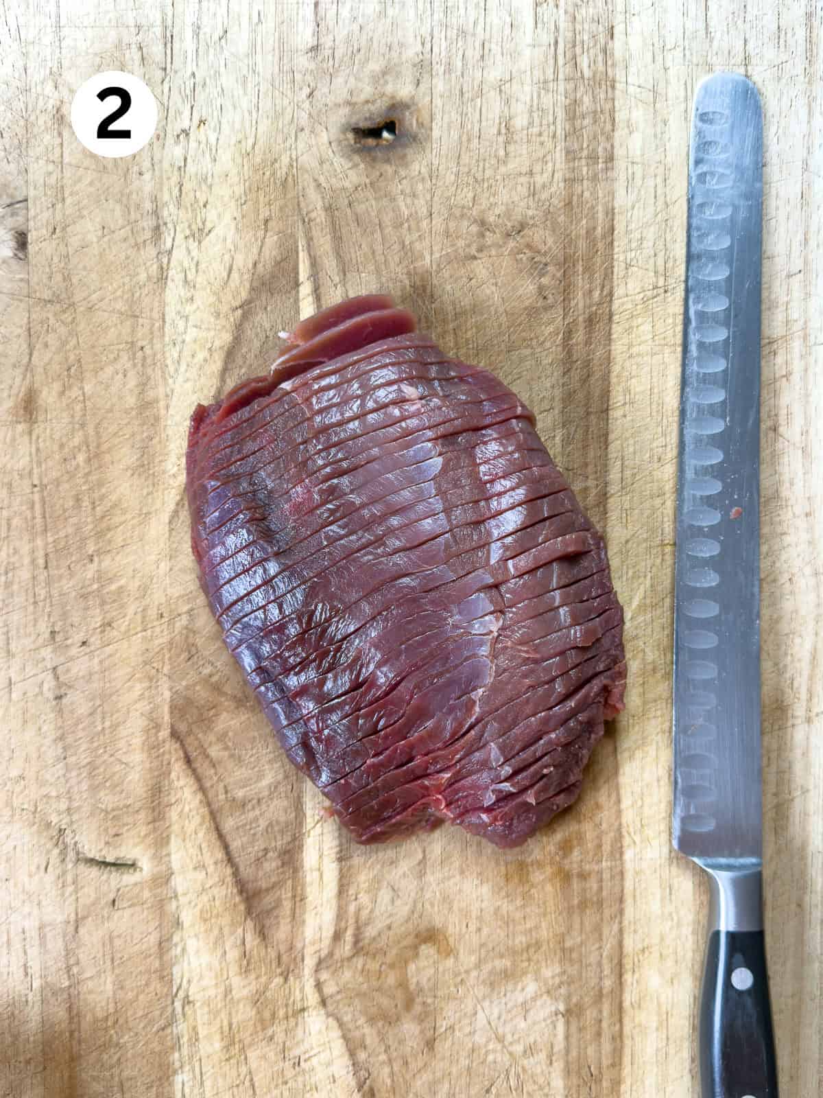 Sliced venison for jerky on a cutting board with a knife.