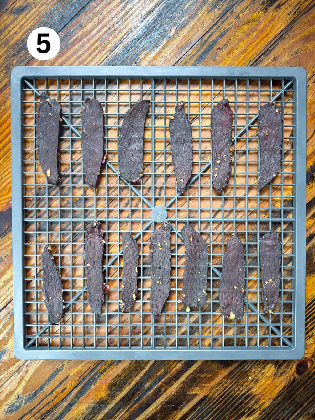 Dried venison jerky on a gray dehydrator rack.