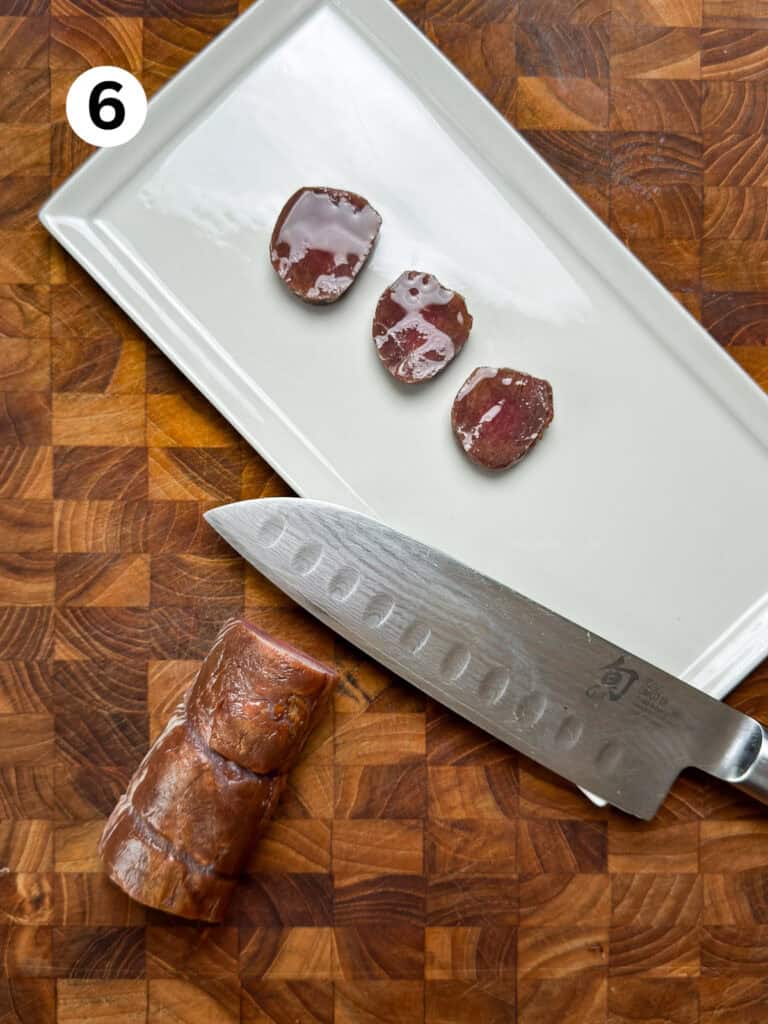 Sliced smoked venison backstrap on a white plate with a knife.