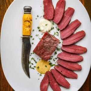 Smoked backstrap recipe on a white plate with a knife.
