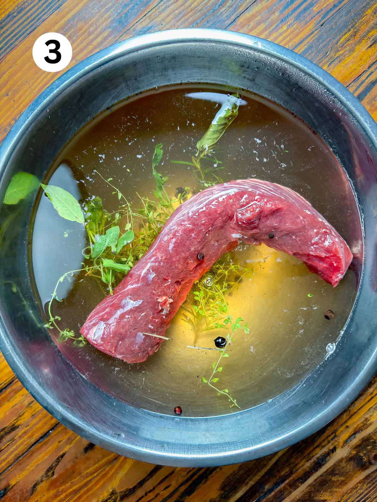 Venison backstrap soaking in a brine on a wooden table.