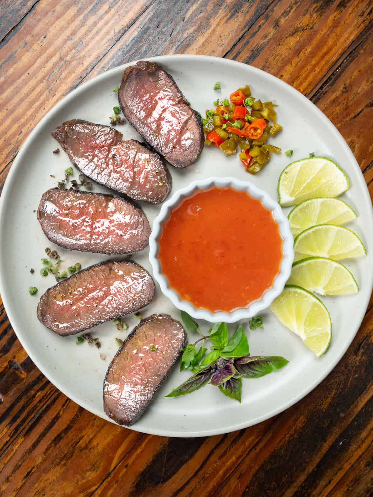 Sliced Thai marinated steak on a plate with sauce and limes.