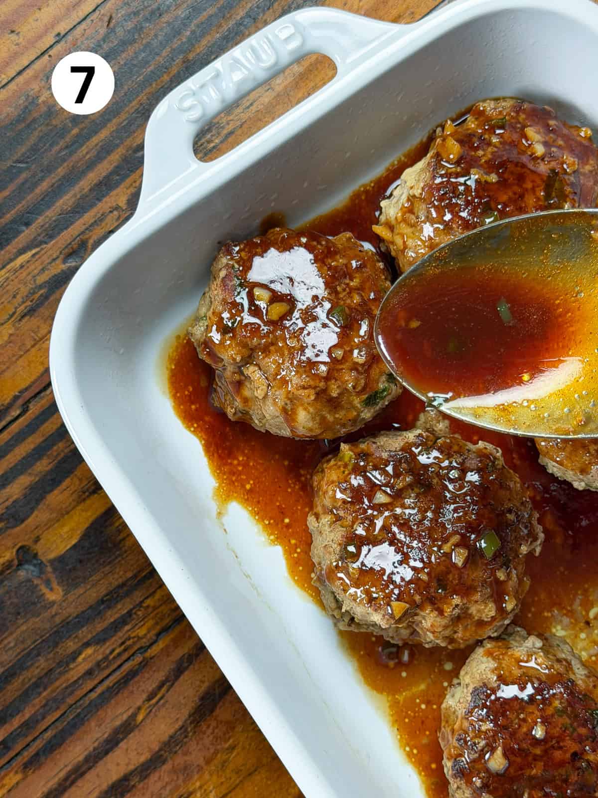 Pouring sauce over venison meatballs in a white dish.