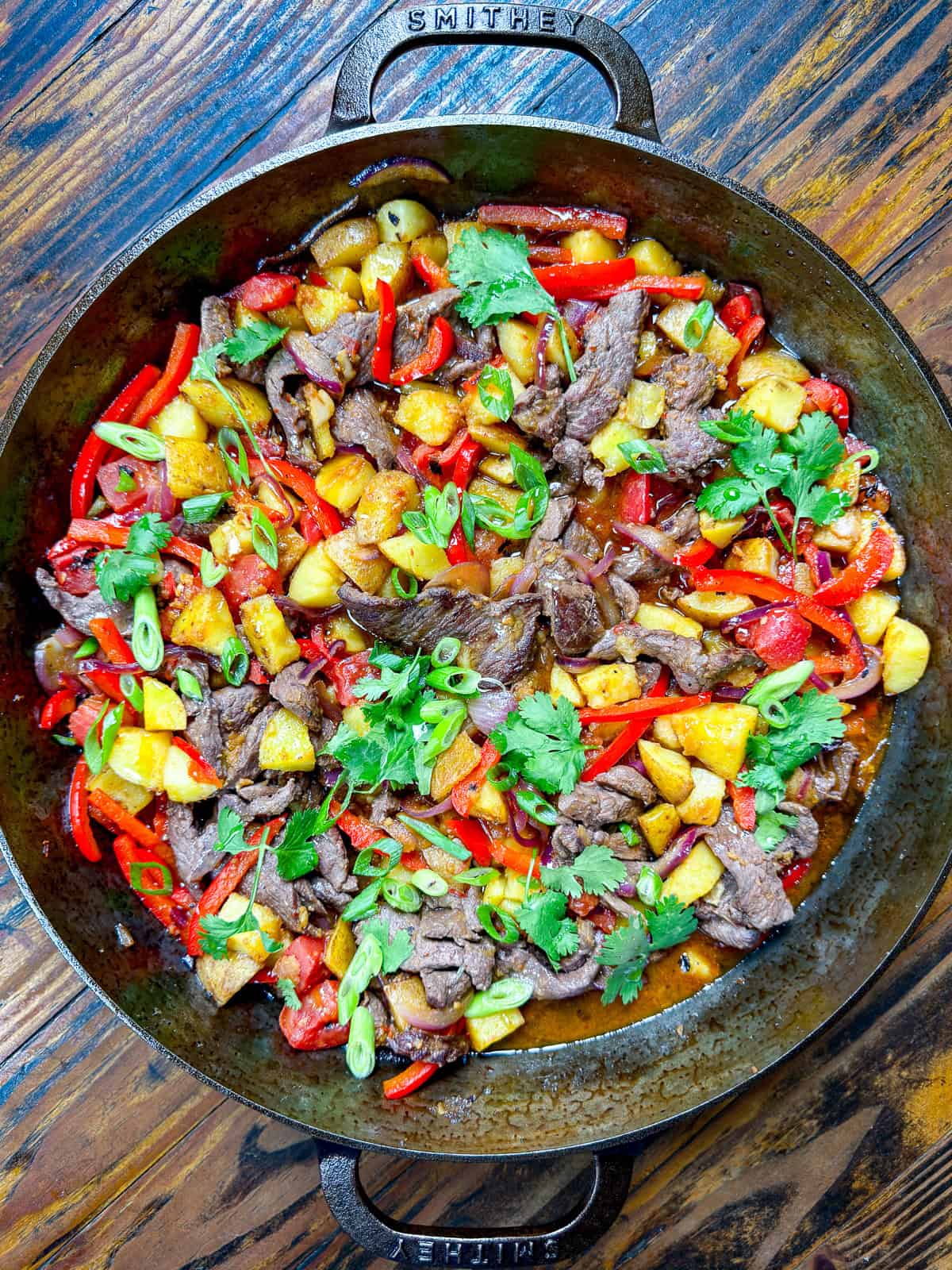 Peruvian venison stir fry in a cast iron pan with cilantro and scallions.
