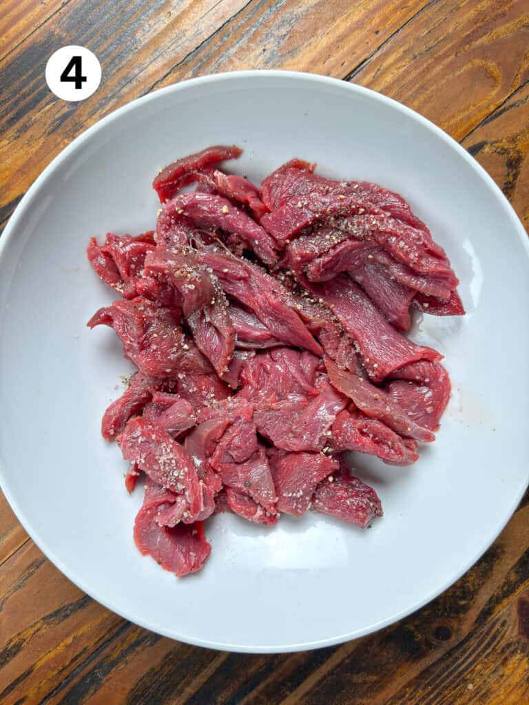 Sliced venison in a white bowl on a wooden table.