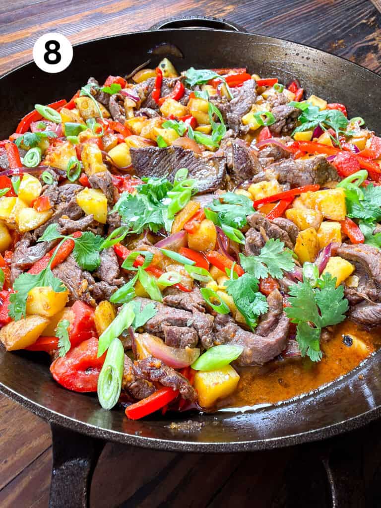 Venison stir fry in a large cast iron pan on a wooden table.