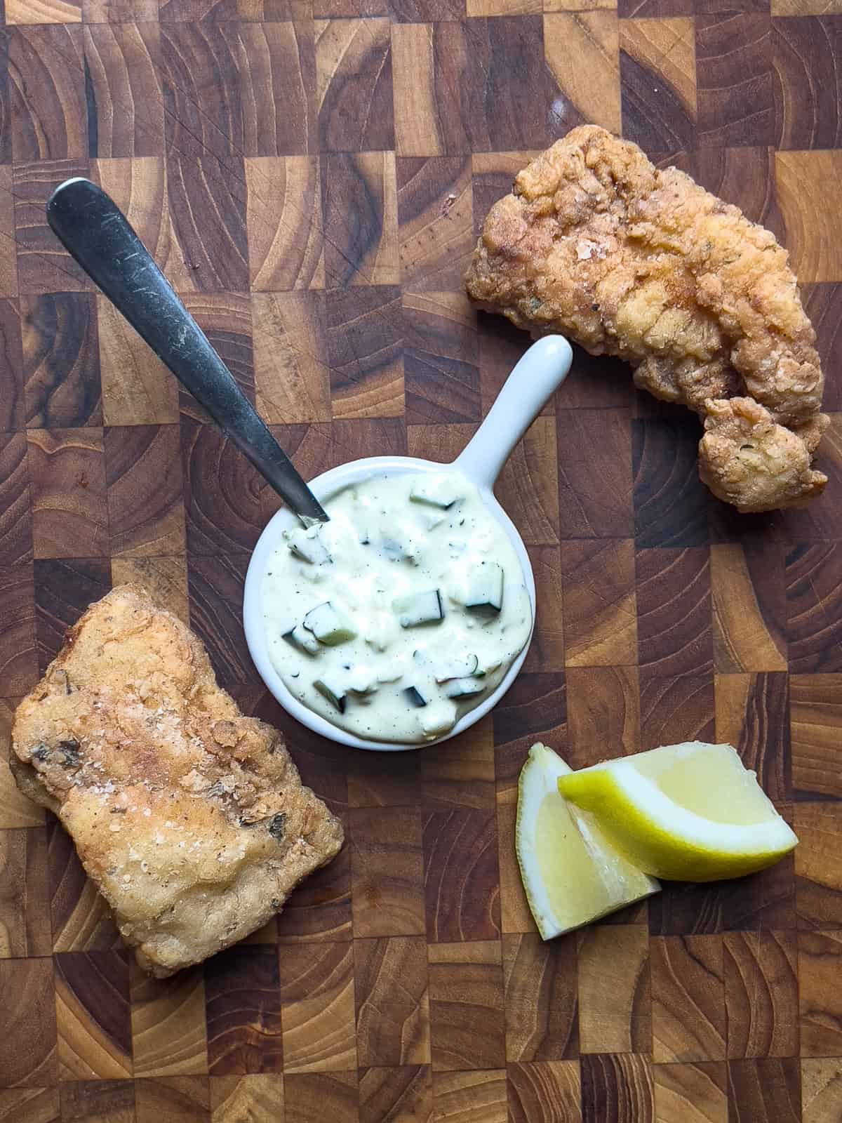 Fried catfish, tartar sauce and lemon on a wooden serving board.