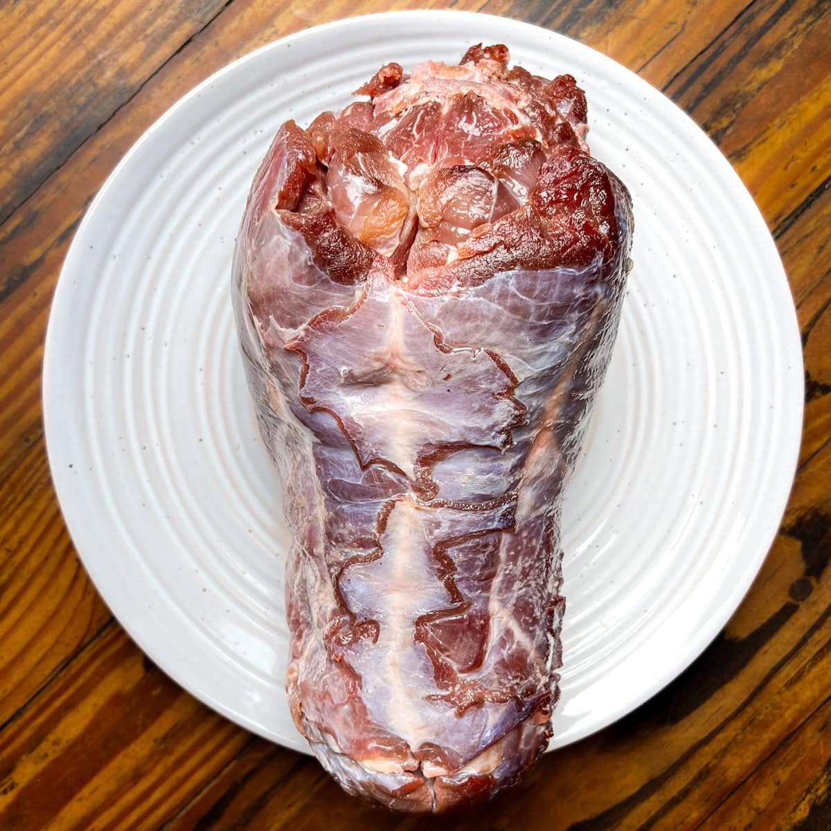 Raw venison neck roast on a white plate.