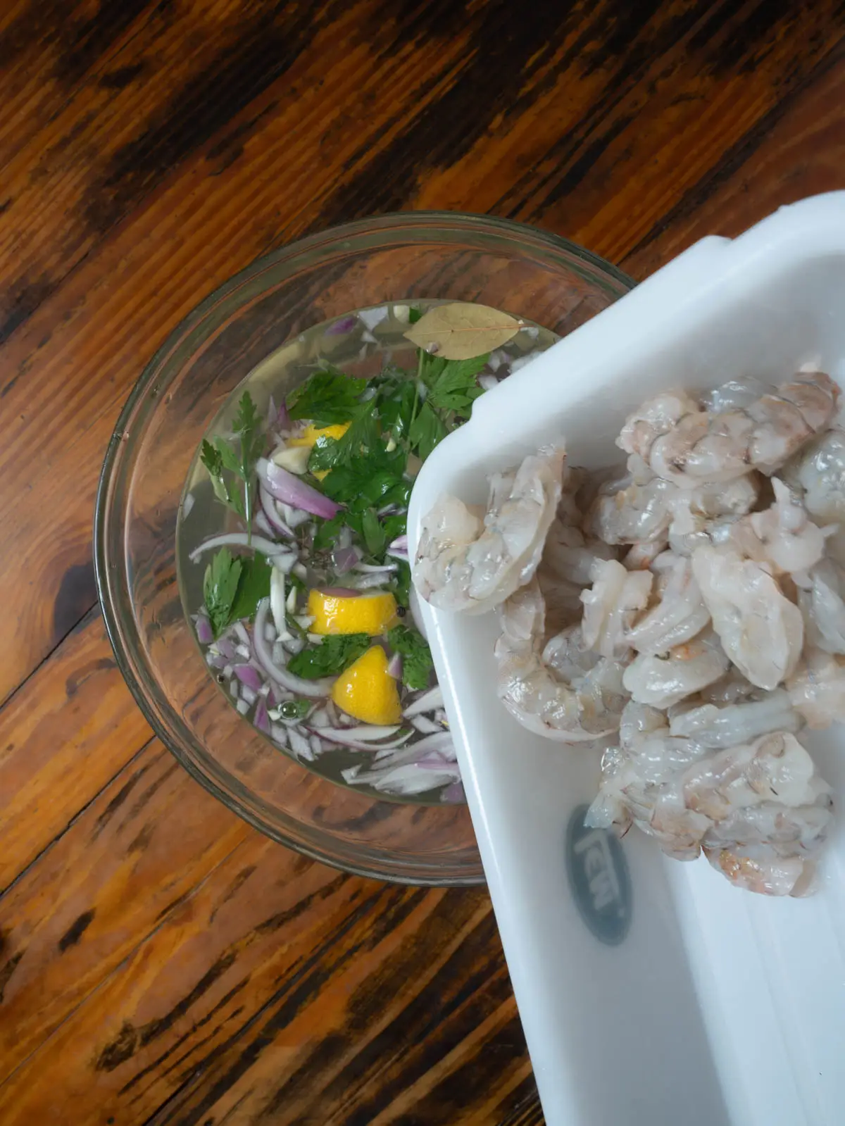Adding shrimp to a brine in a bowl.