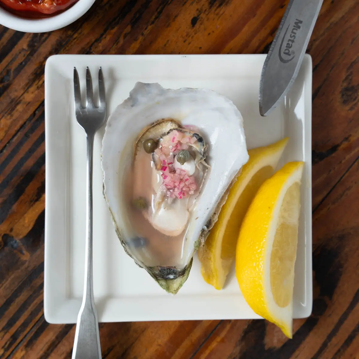 Steamed oyster on a plate with lime and mignonette.