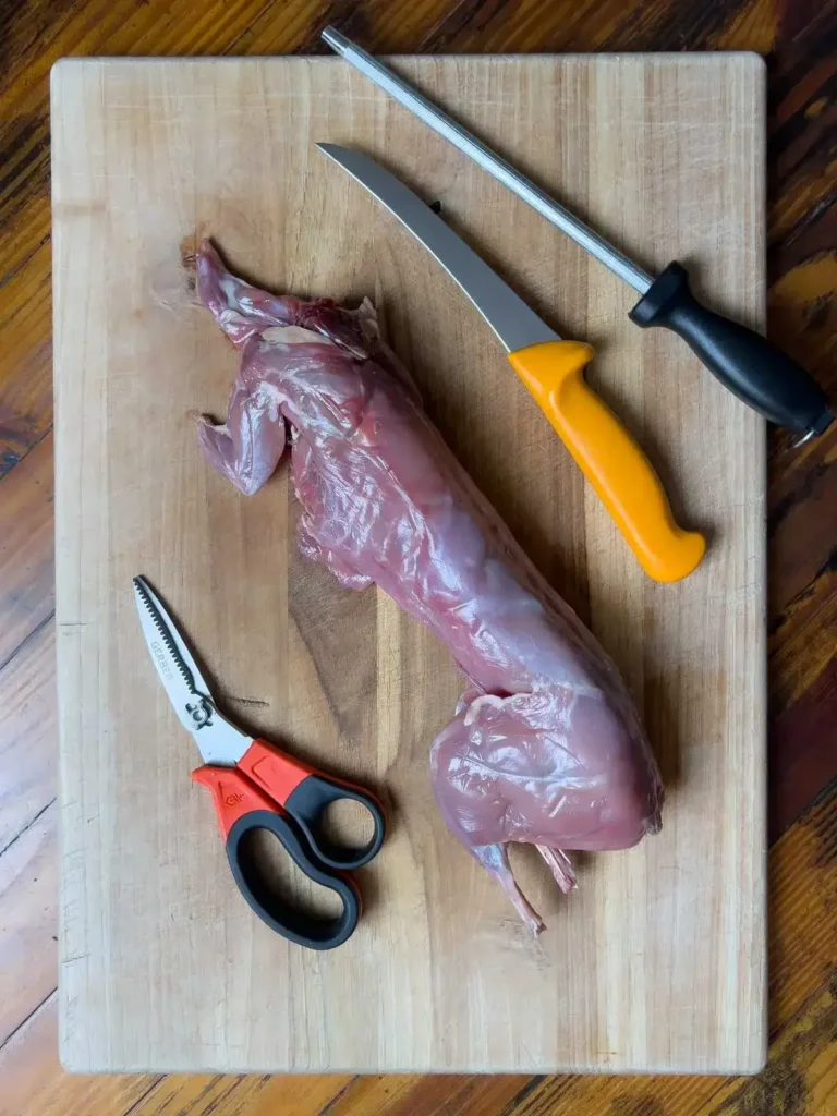 Wild rabbit on a cutting board with shears, knife and honing steel.