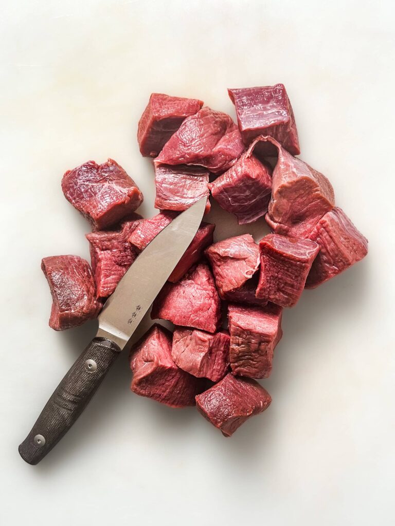 Deer meat cut into cubes with a knife resting on top of the meat.