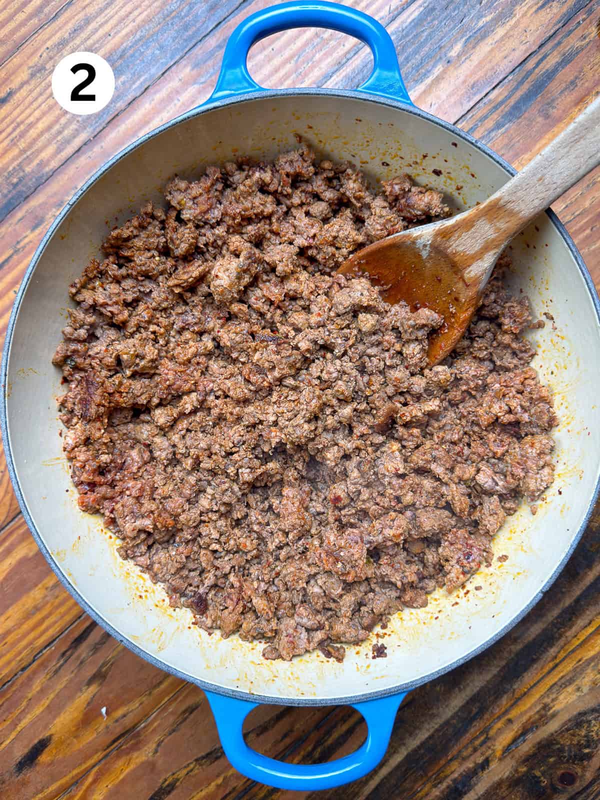 Browned venison in a blue pot with a wooden spoon.