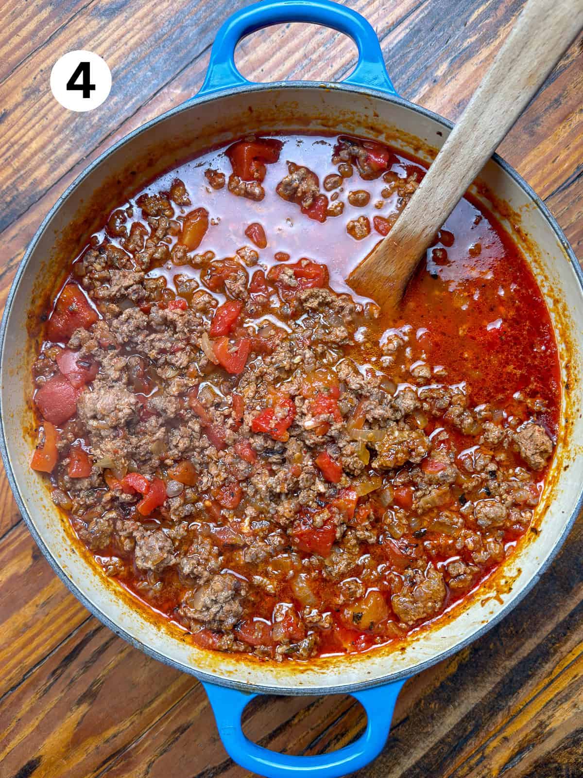 Venison chili in a pot with a wooden spoon before adding the beans.
