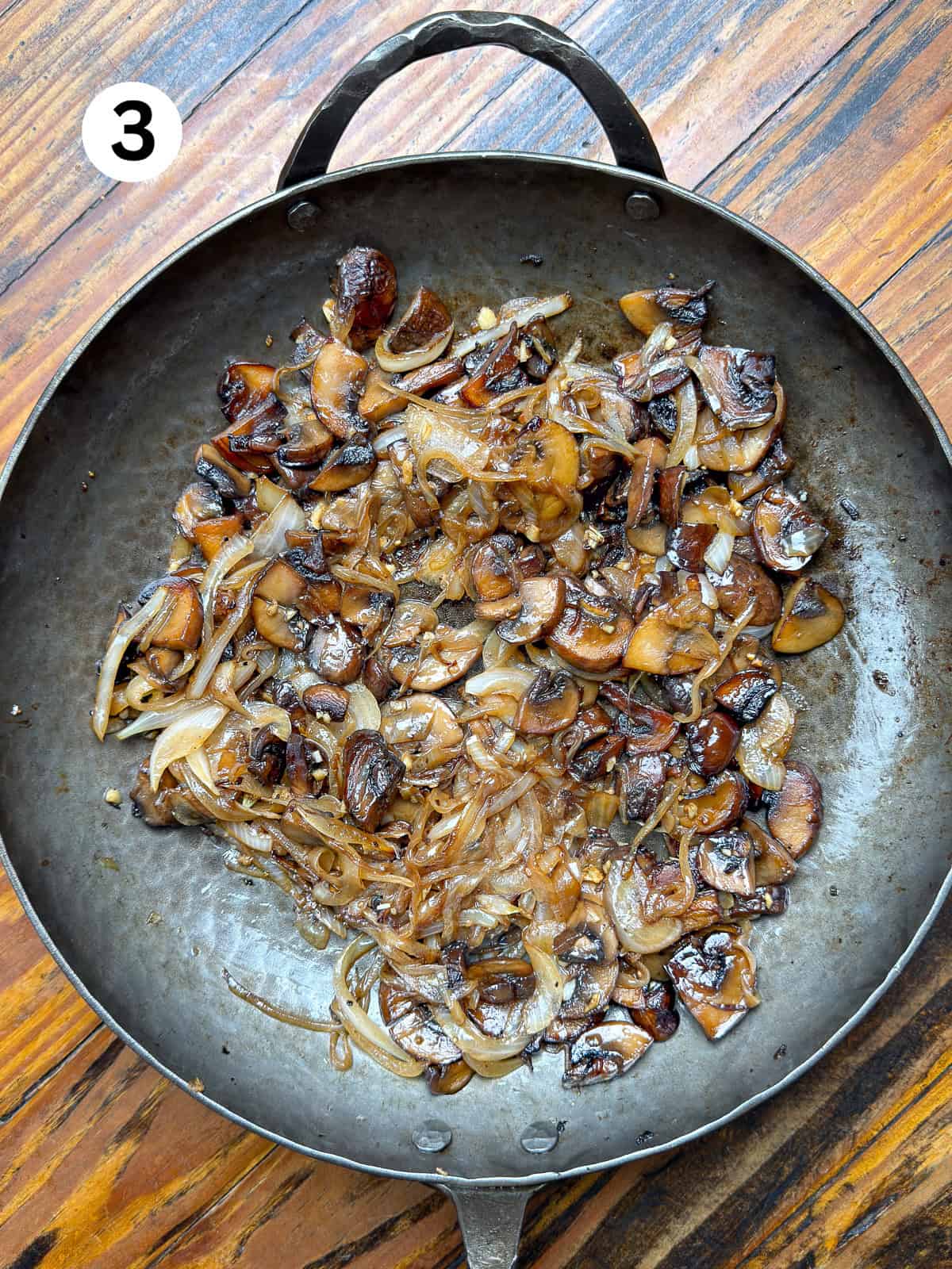 Thai-Fish-Sauce-Dressing Browned mushrooms and onions. in a carbon steel pan on a wooden table.