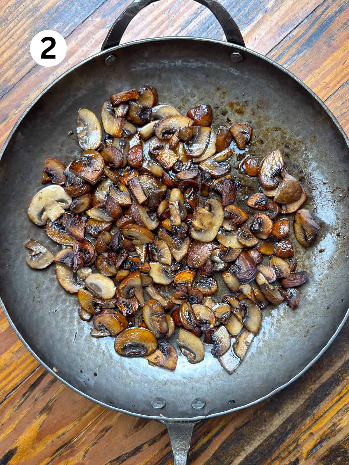 Browned mushrooms in a carbon steel pan on a wooden table.