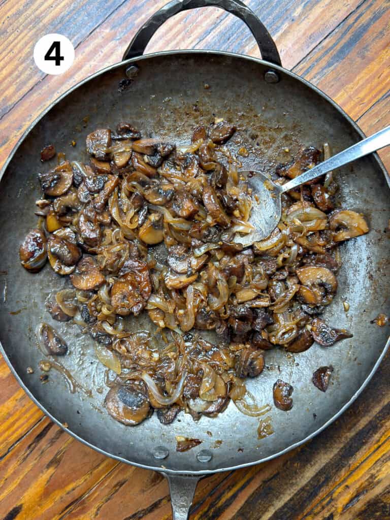 Deglazed mushrooms and onions in a carbon steel pan on a wooden table.