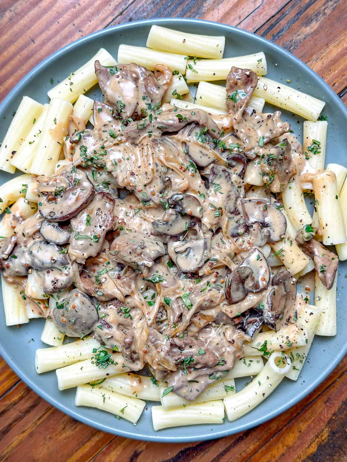 Venison stroganoff and pasta on a gray plate sitting on a wooden table.