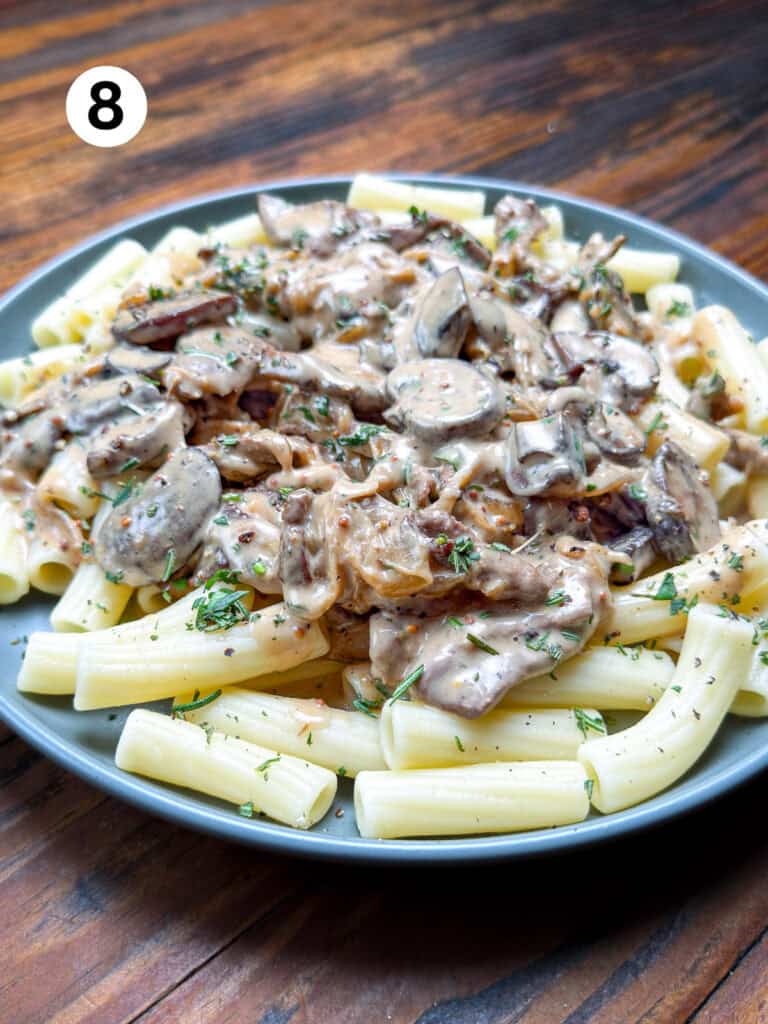 Venison stroganoff on a gray plate with pasta, fresh herbs and black pepper.