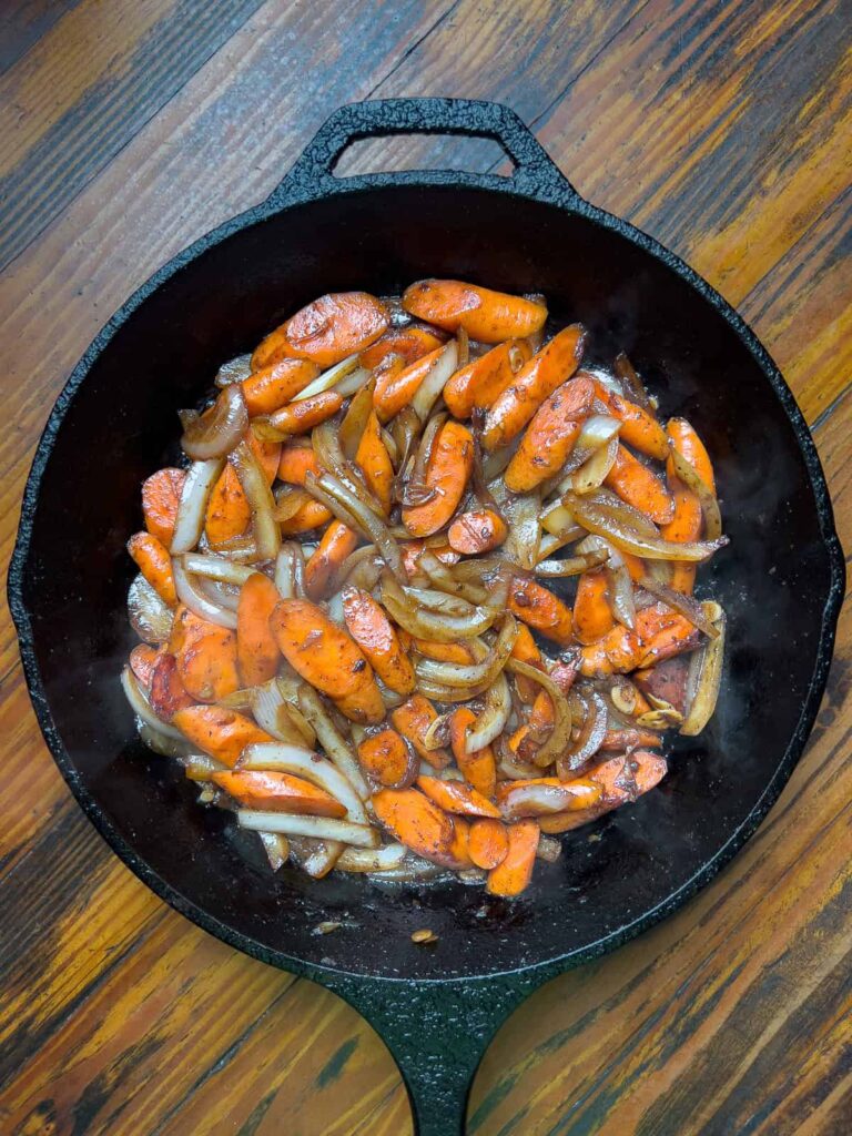 Sautéed carrots and onions in a cast iron pan.