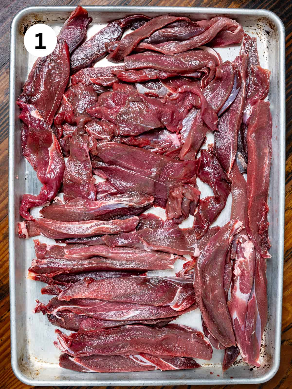 Venison cut into strips on a baking tray.