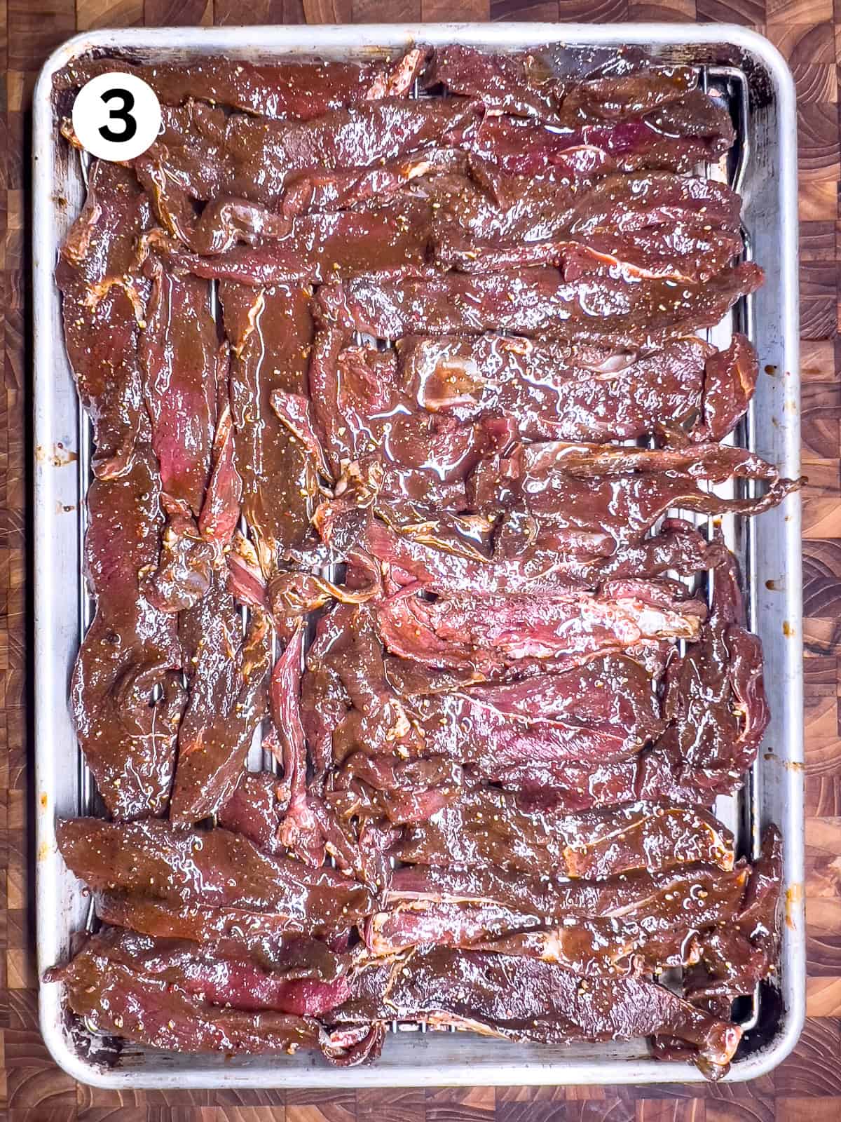 Raw marinated venison jerky sitting on a a wire baking rack.