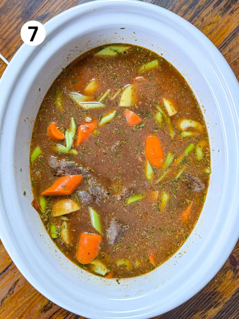 Uncooked venison stew in a white slow cooker.