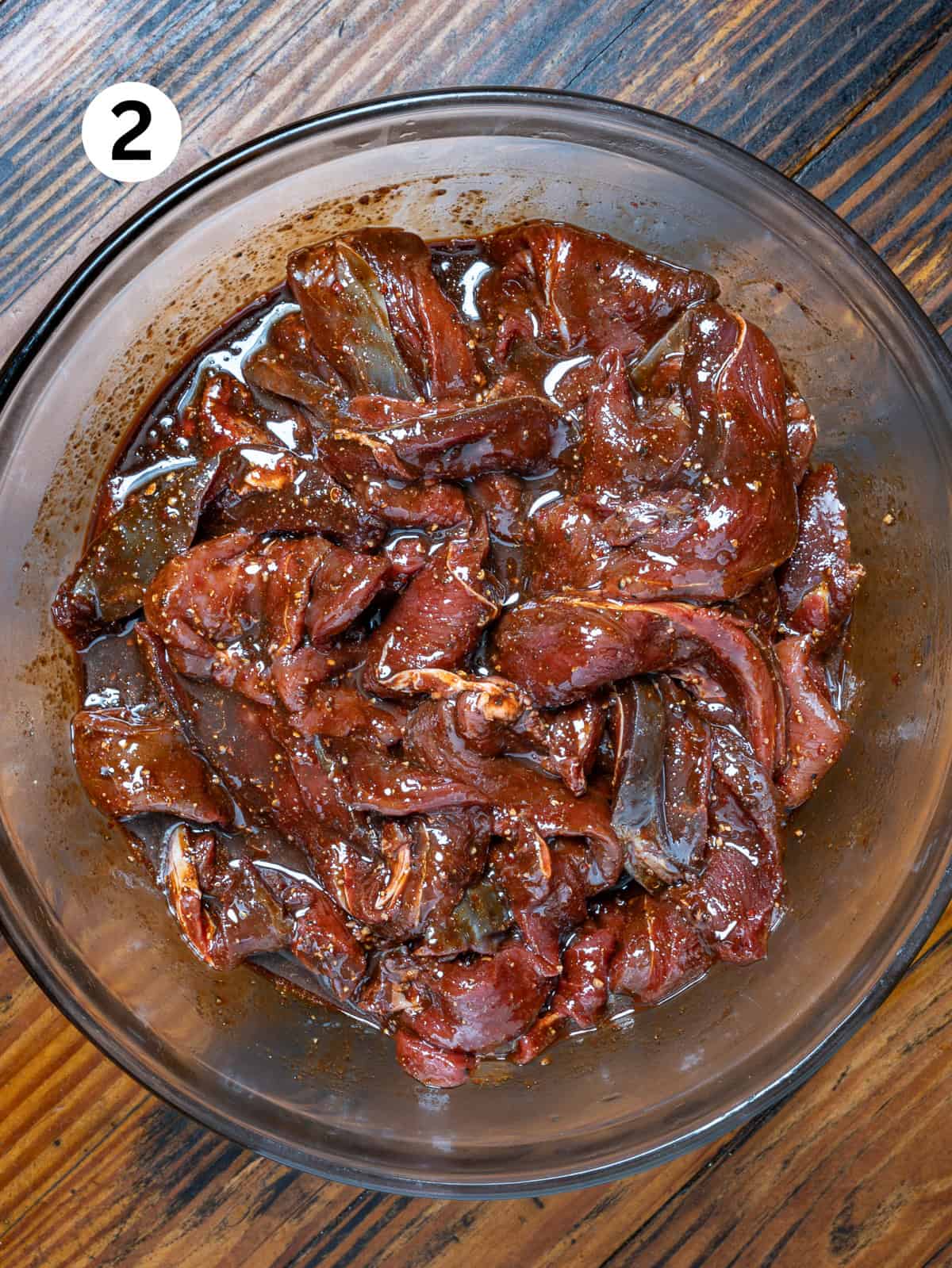 Venison marinating in a smoked venison jerky marinade on a wooden table.