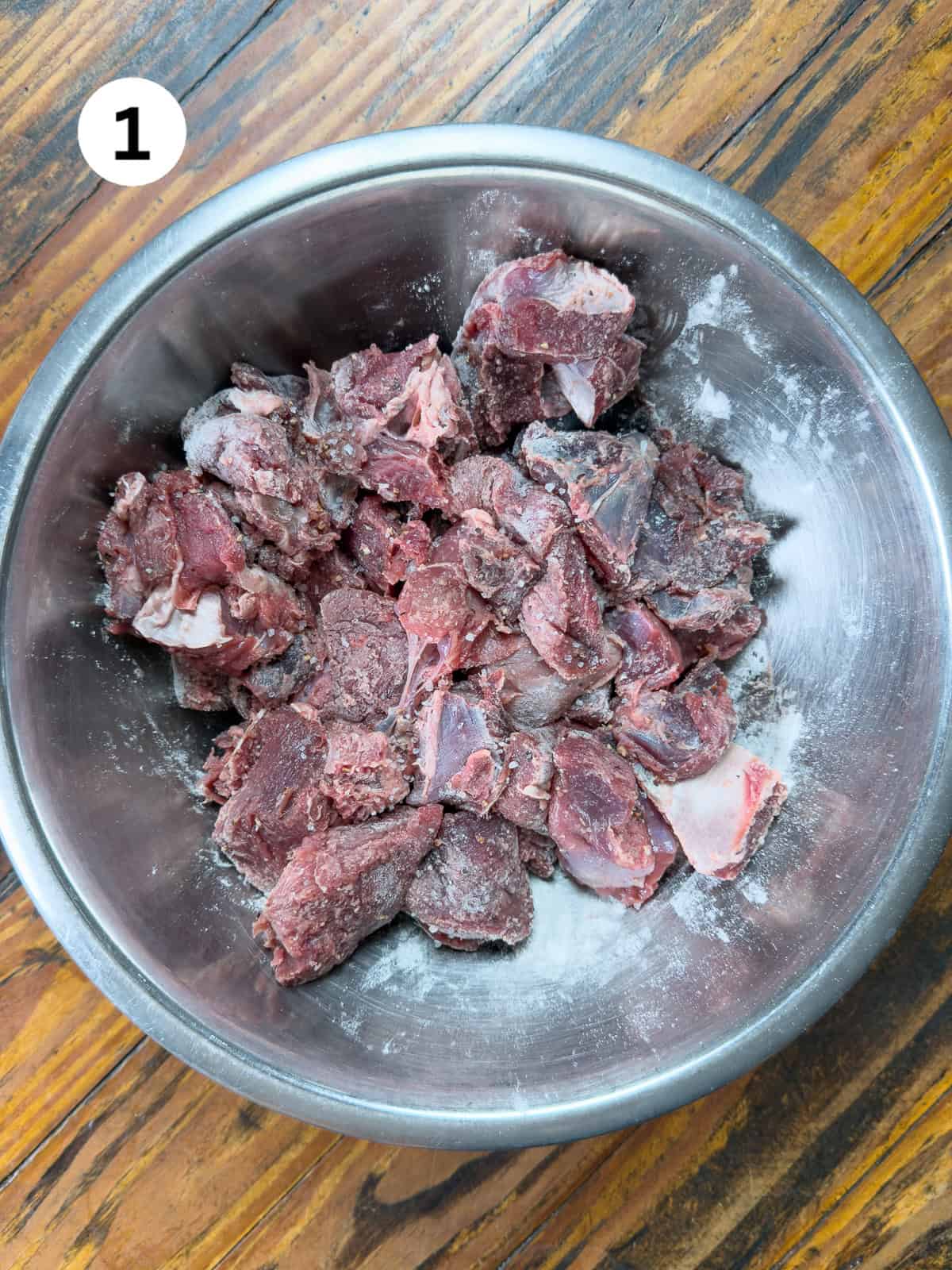 Venison stew meat in a bowl with salt, pepper and flour.