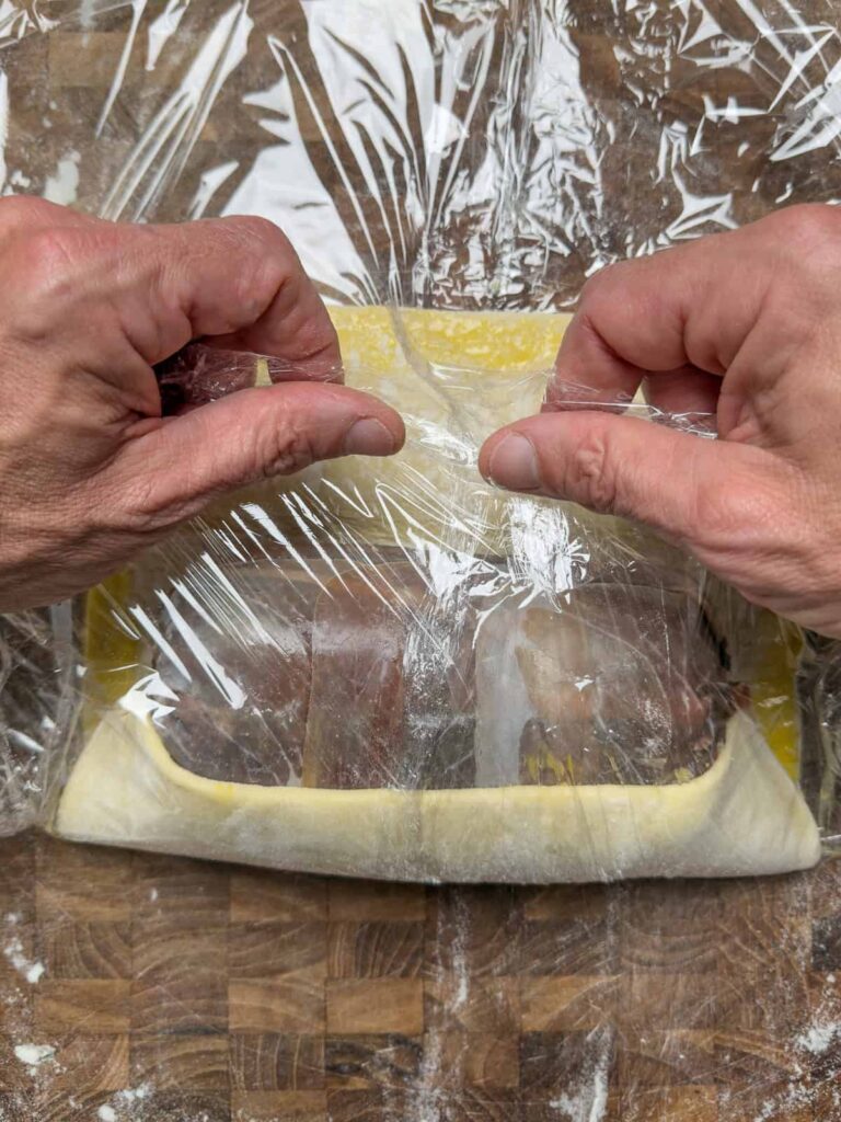 rolling a venison wellington in plastic wrap.