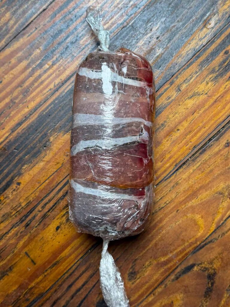 Venison rolled in prosciutto and mushrooms wrapped in plastic wrap.
