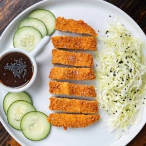 Fried pork tonkatsu on a plate with sauce and vegetables.