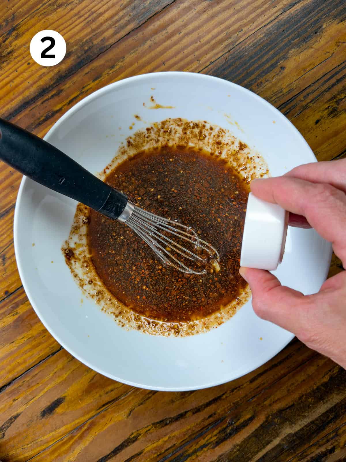 Adding dry ingredients to a Thai steak marinade in a white bowl.
