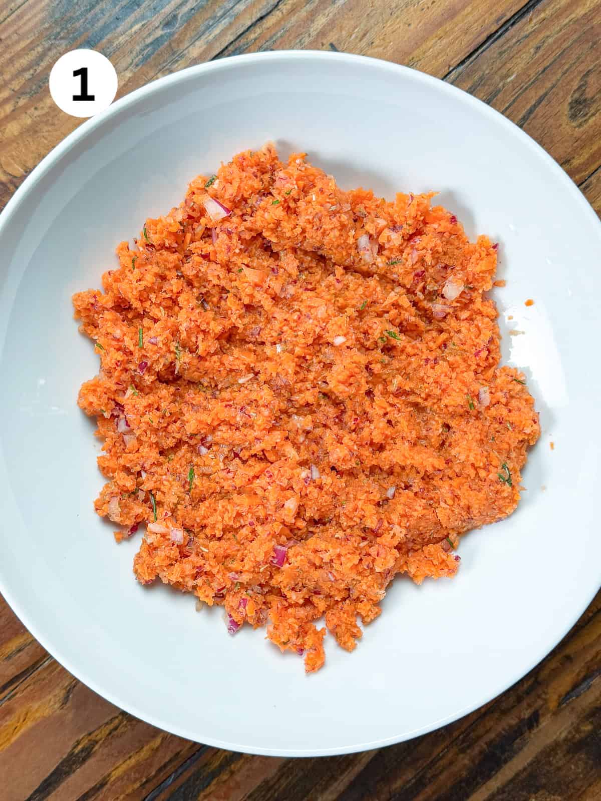 FInely chopped carrots, onions and garlic in a white bowl.