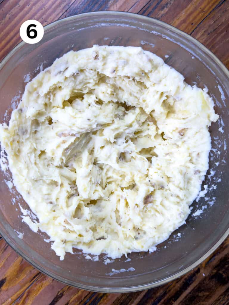 Mashed potatoes in a glass bowl on a wooden table.