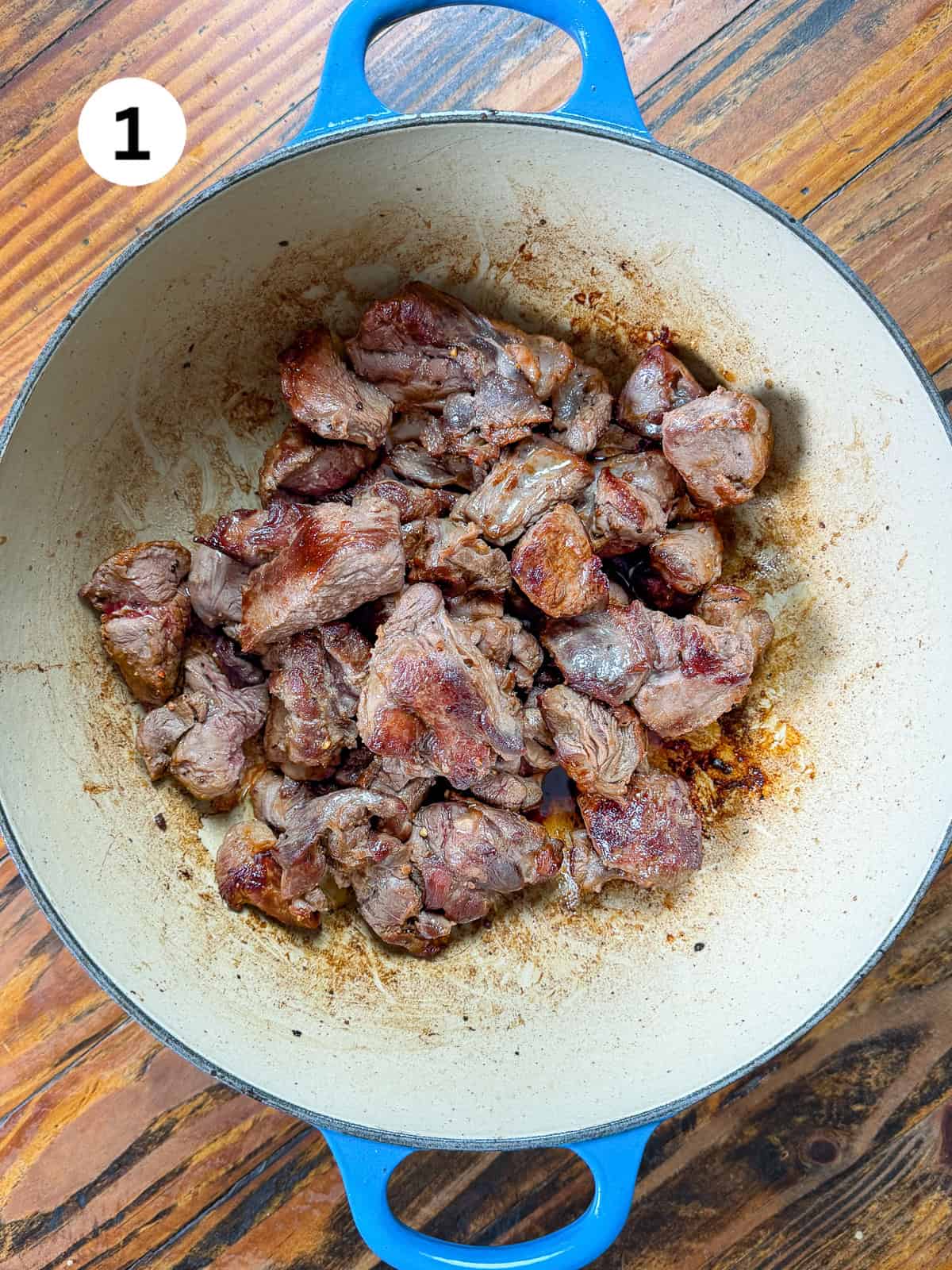 Seared venison stew in a pot on a wooden table.