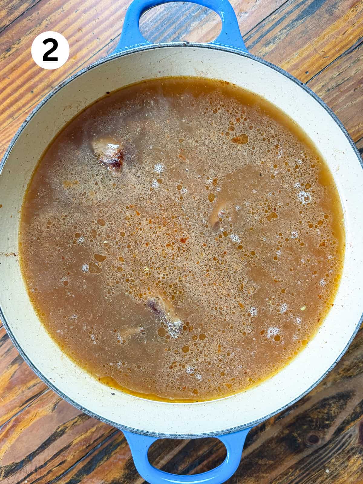 Venison stew meat and stock in a pot on a wooden table.