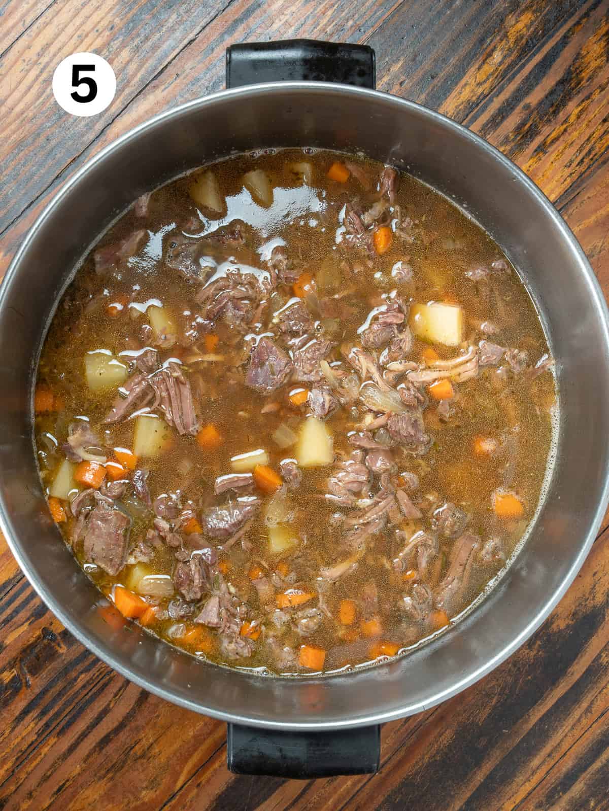 Venison stew in a stainless pot on a wooden stable.