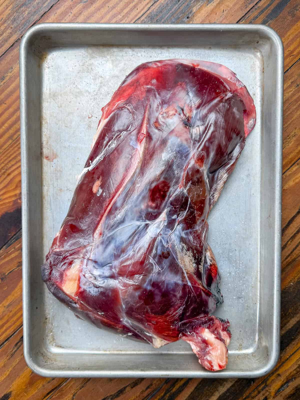 Dry aged venison shoulder roast on a baking sheet.