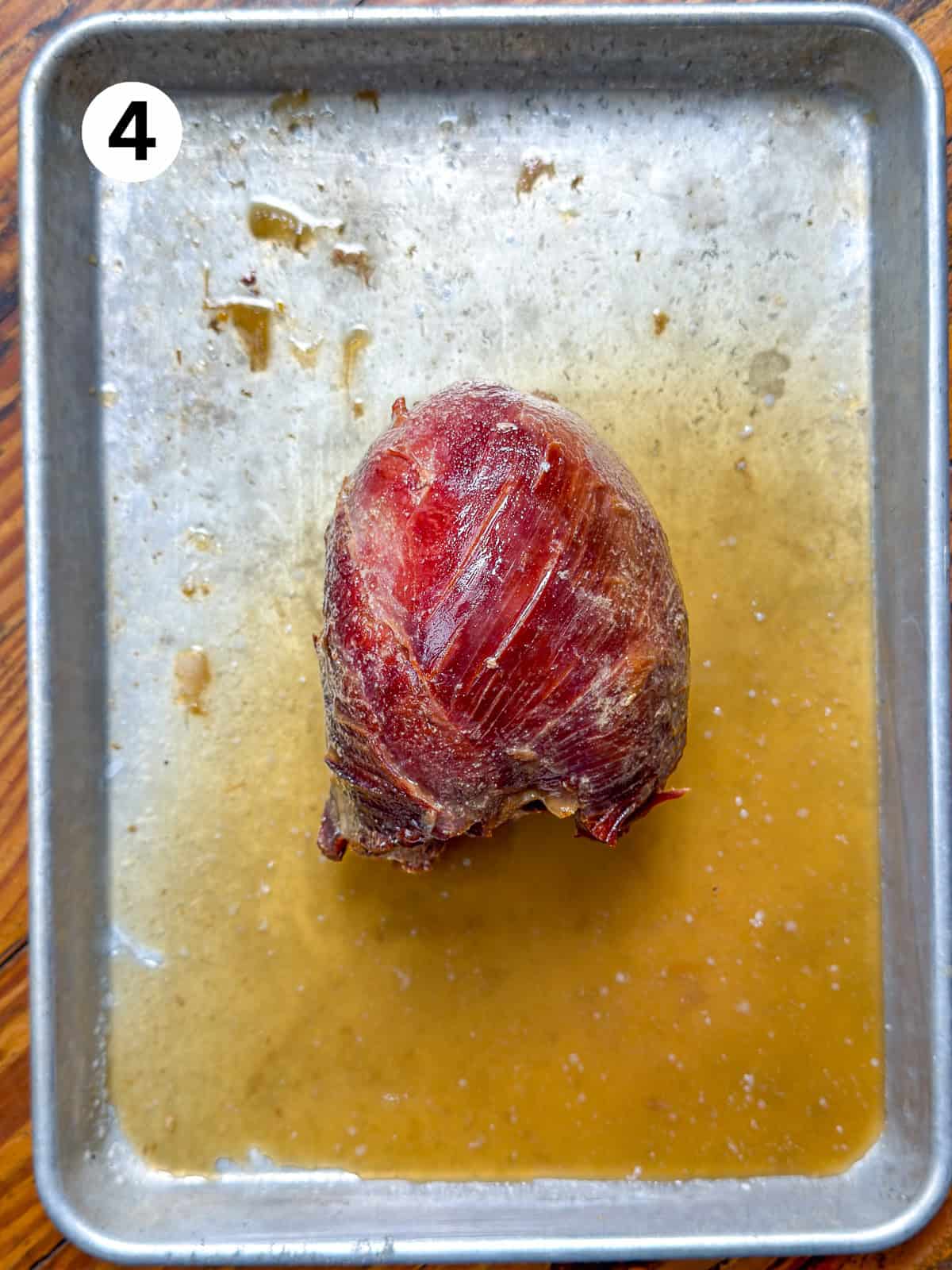 Lightly smoked venison roast on a baking pan with braising liquid.
