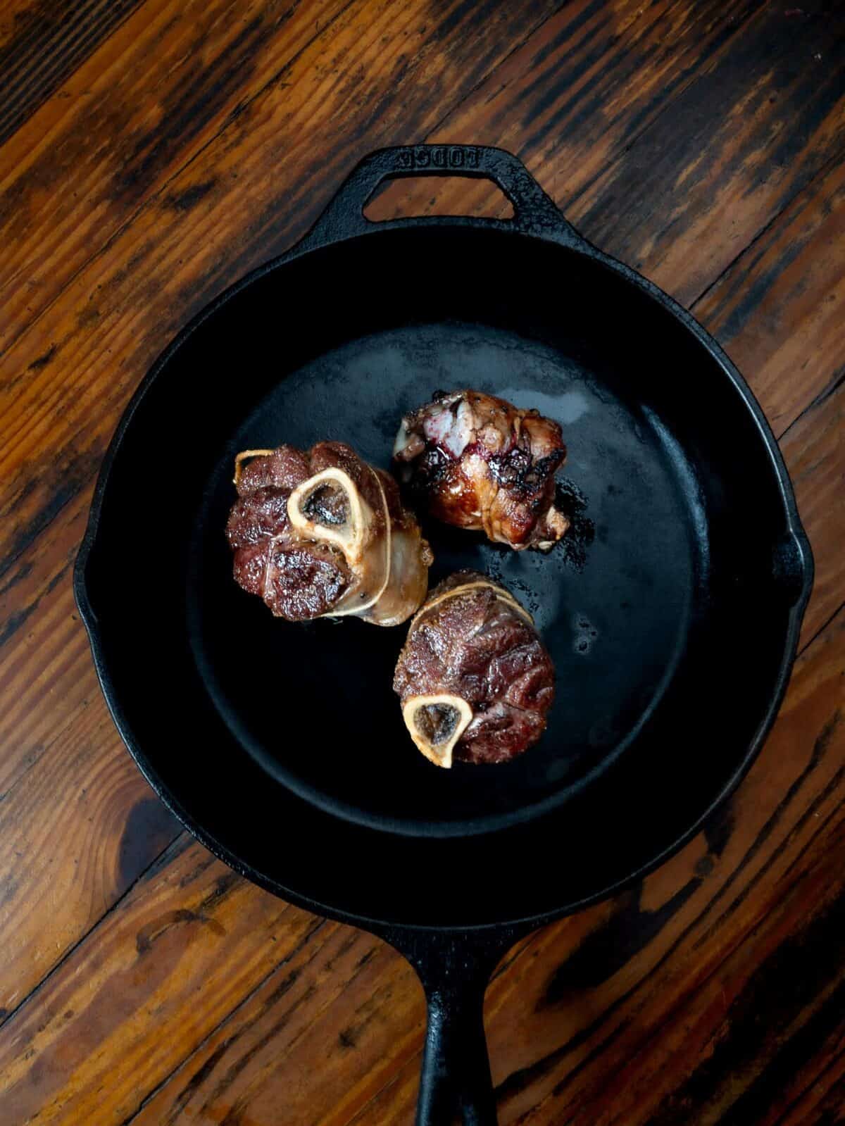Seared venison shanks in cast iron pan.